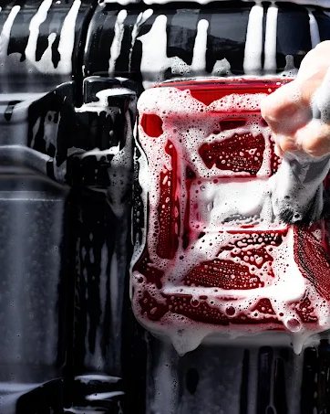 A soapy wash mitt working suds across the glossy black panel of a vehicle