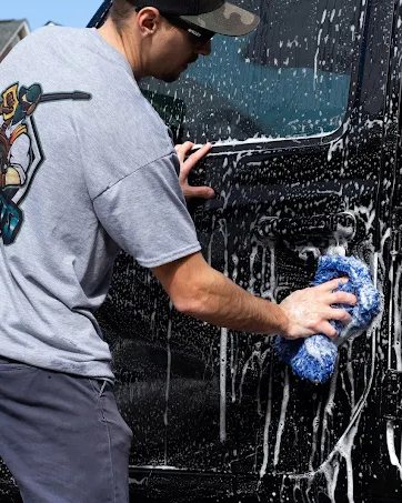 Hand washing the side of a foamed-up black truck